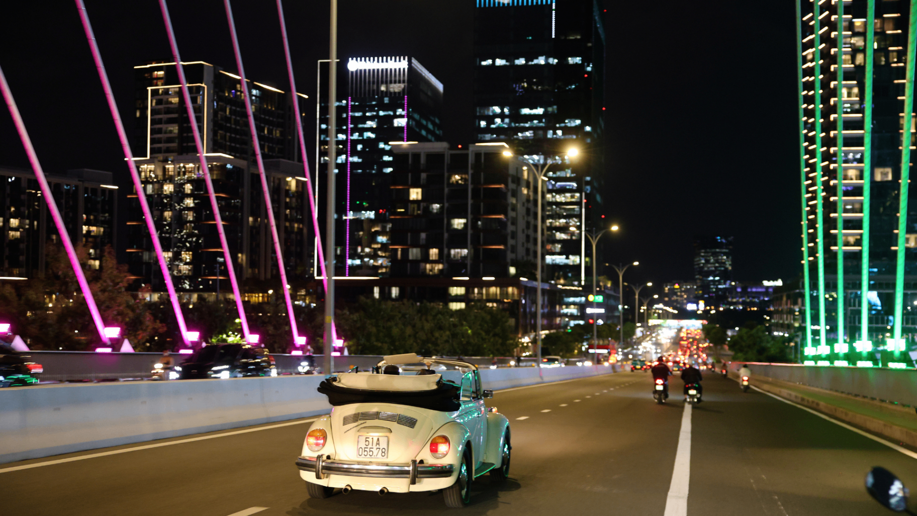 Retro car crossing a brightly lit Saigon bridge at night.